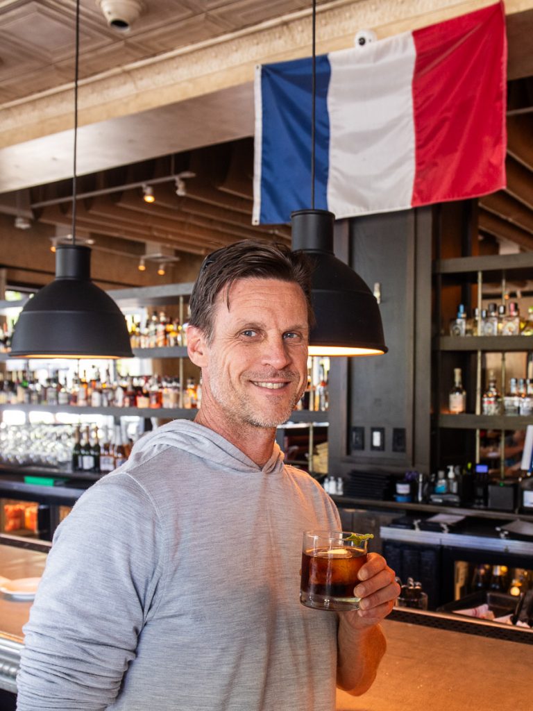 Man drinking a cocktail at a bar under a French flag