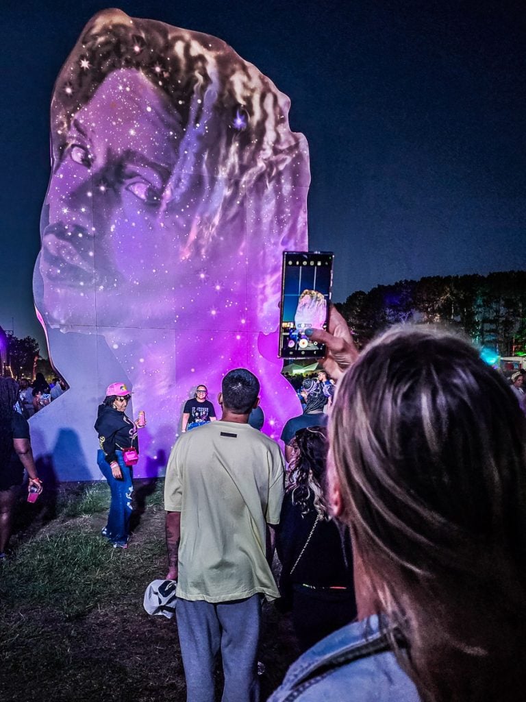 People at a music festival taking a phot of a J Cole installation.
