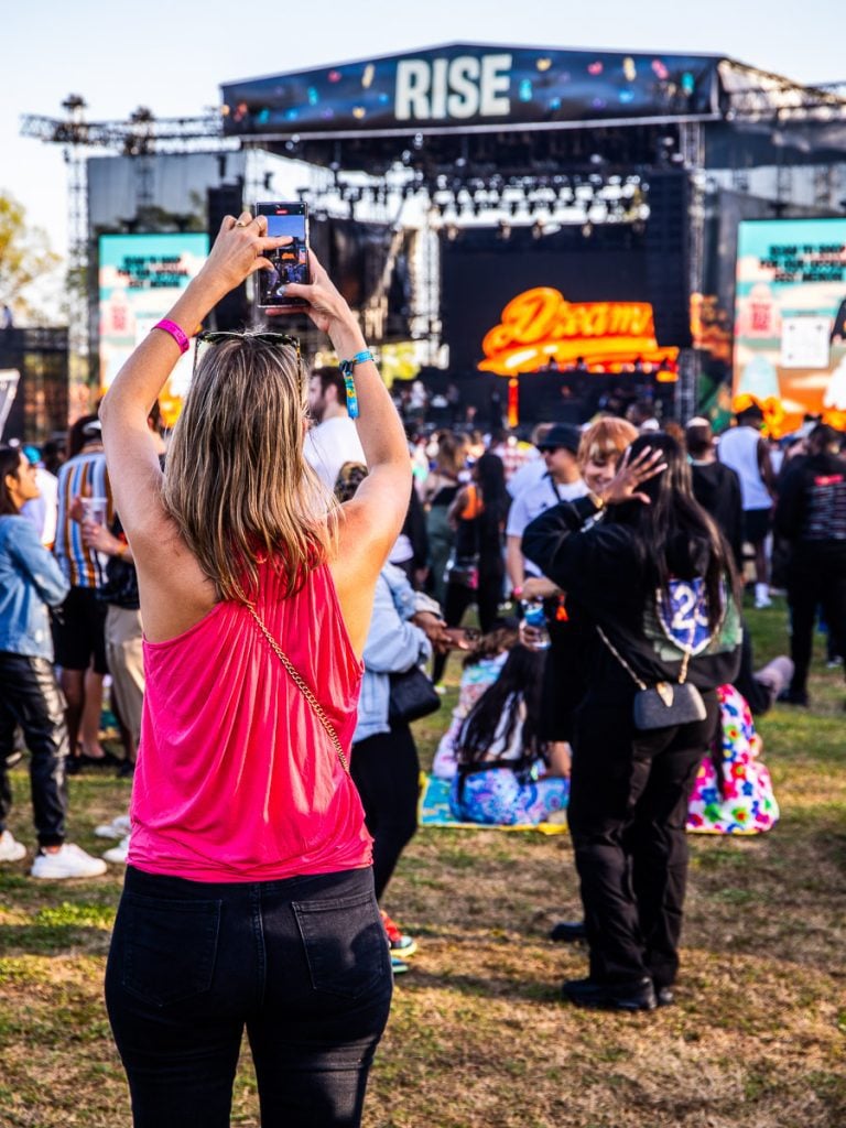 A lady at a music festival taking a phot of the stage.