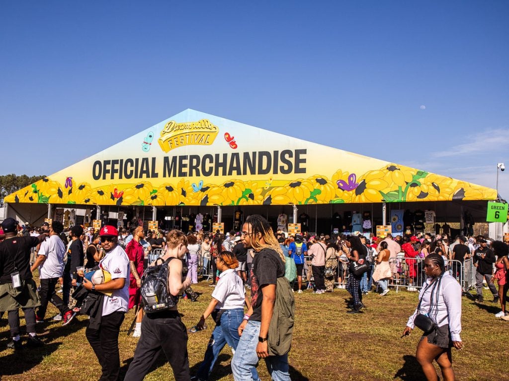 People at a music festival buying merchandise under a tent.