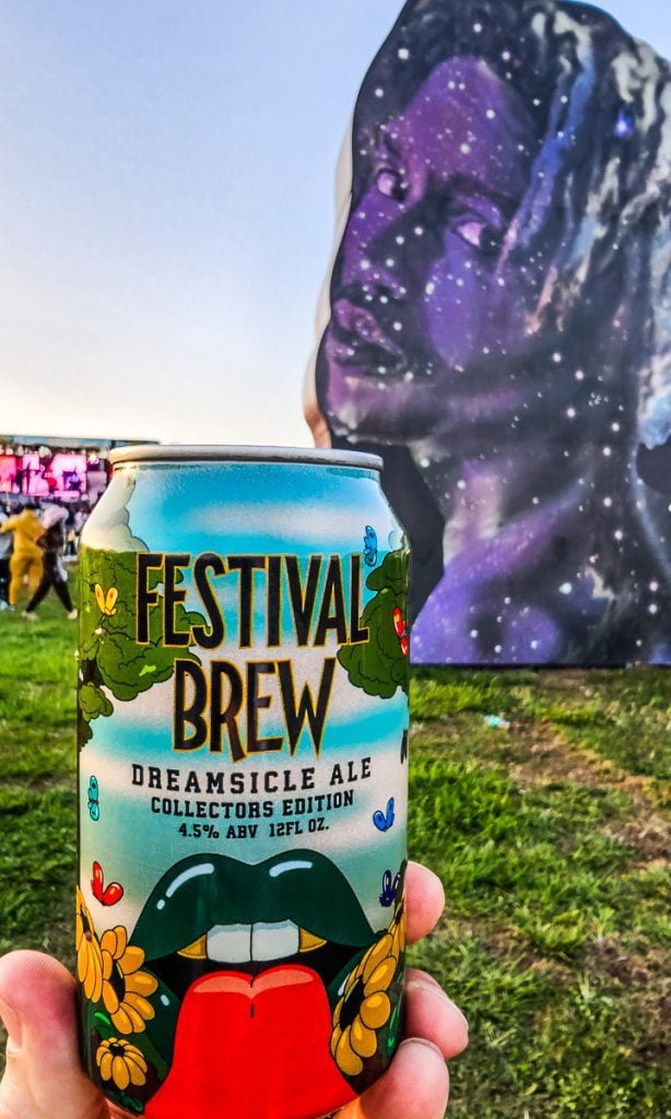 A hand holding up a can of beer at a music festival.