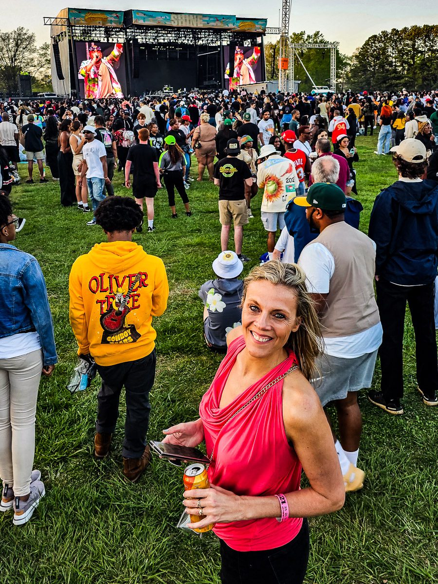 A woman at a music festival with drink and phone in hand.