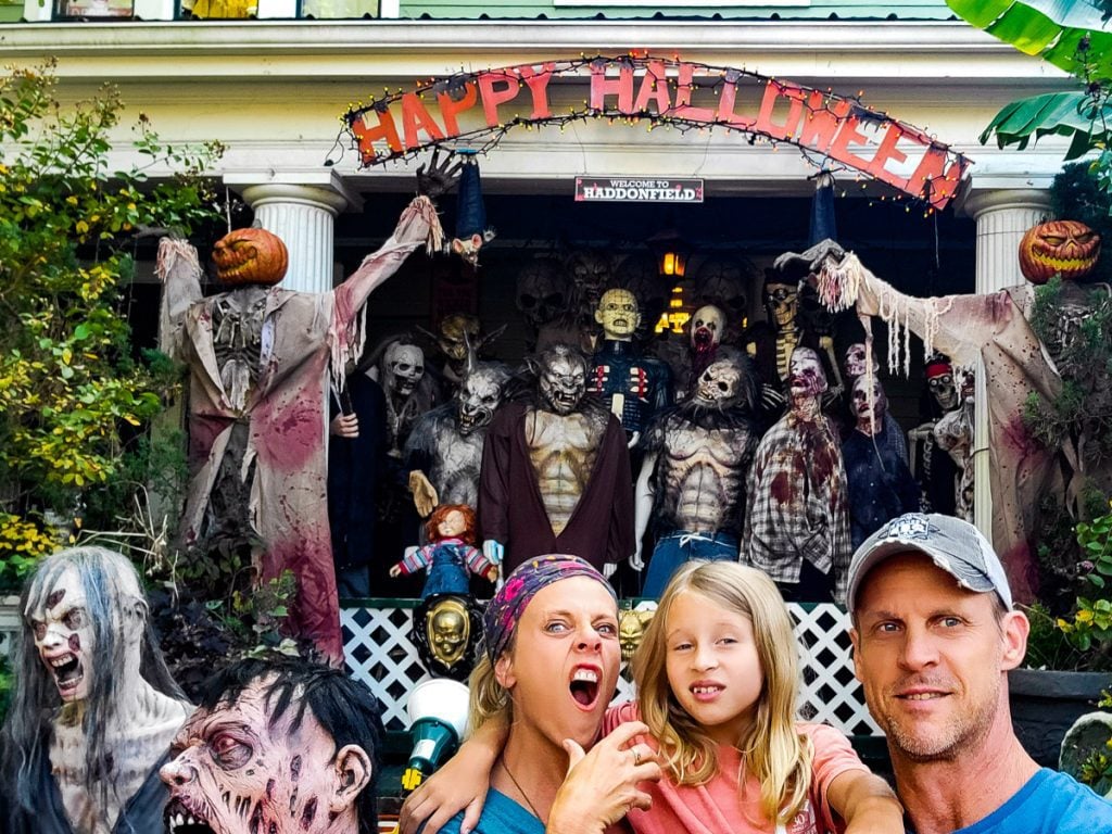 Mom, dad and daughter surrounded by Halloween decorations outside a house.