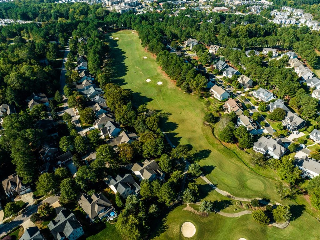 Aerial photo of houses in a neighborhood with green trees and a golf course.
