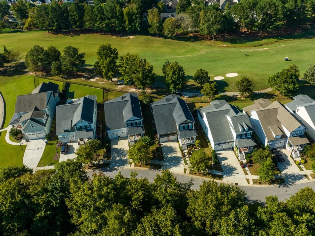 Aerial photo of houses in a neighborhood with green trees and a golf course.