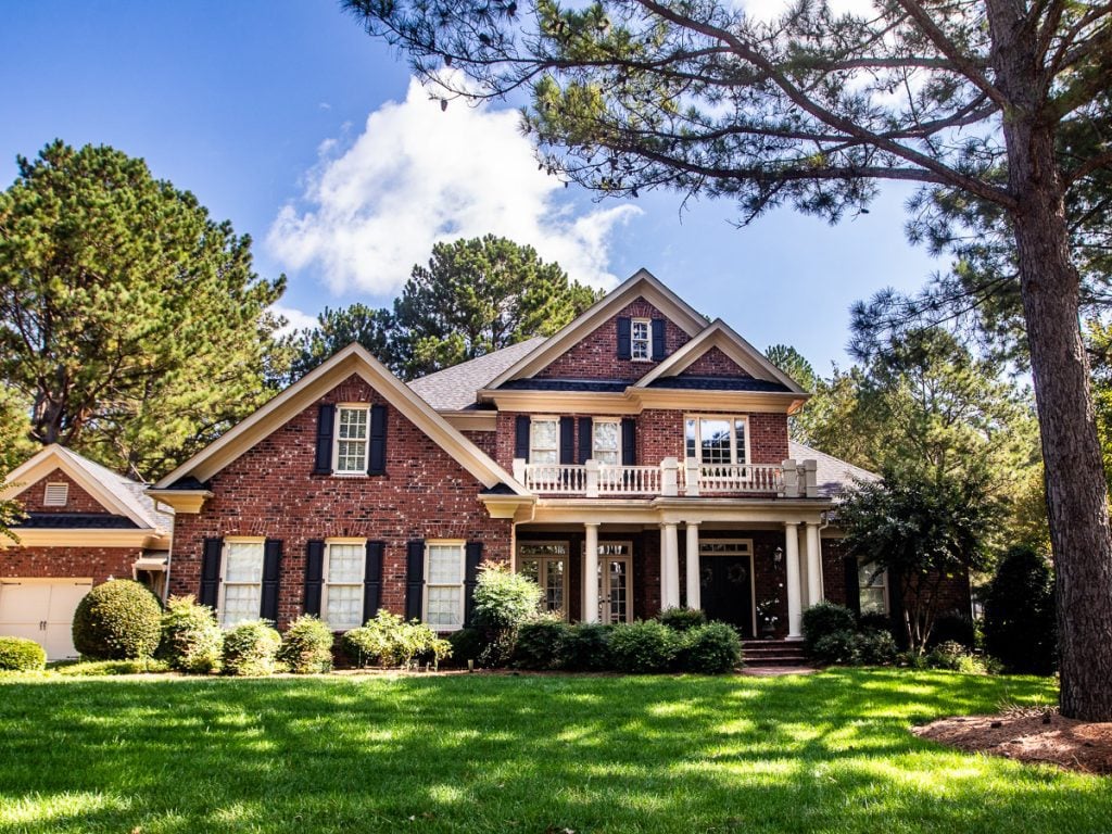 Front of a brick home surrounded by trees and green grass.