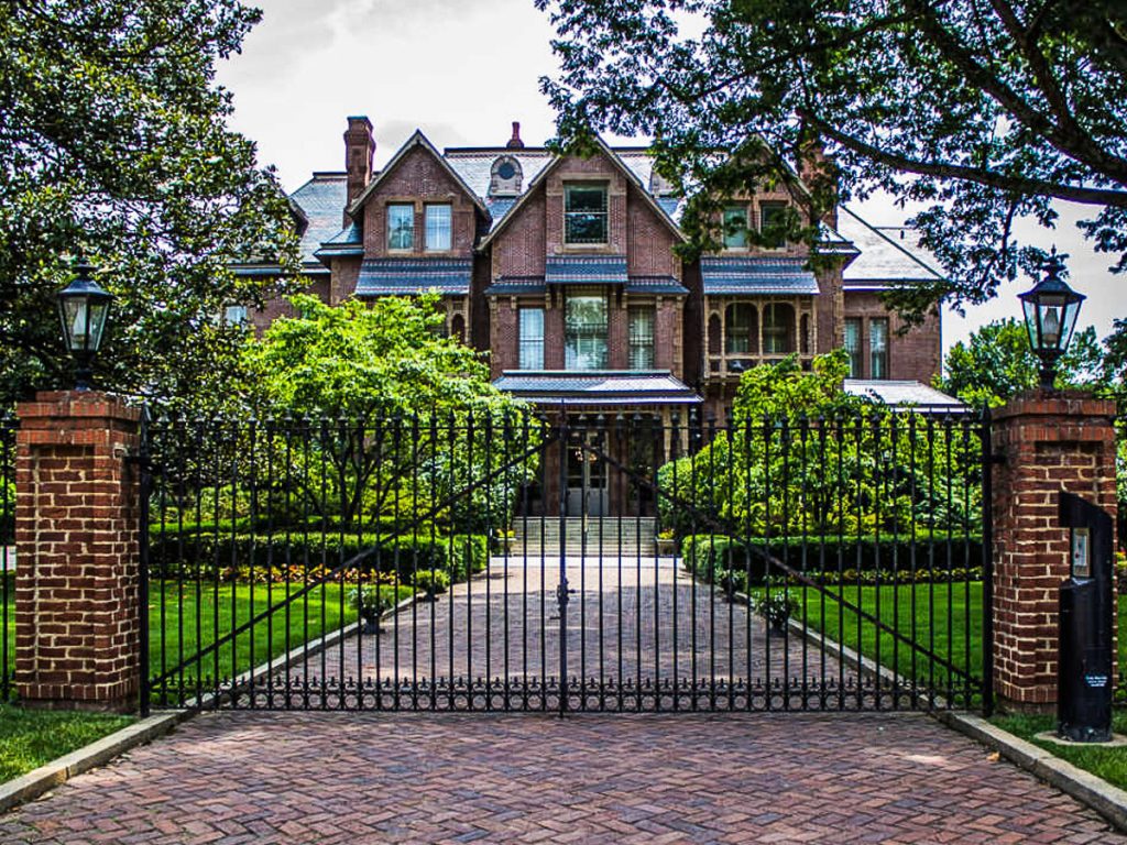 Brick path and metal gate that leads to a two-story brick mansion.