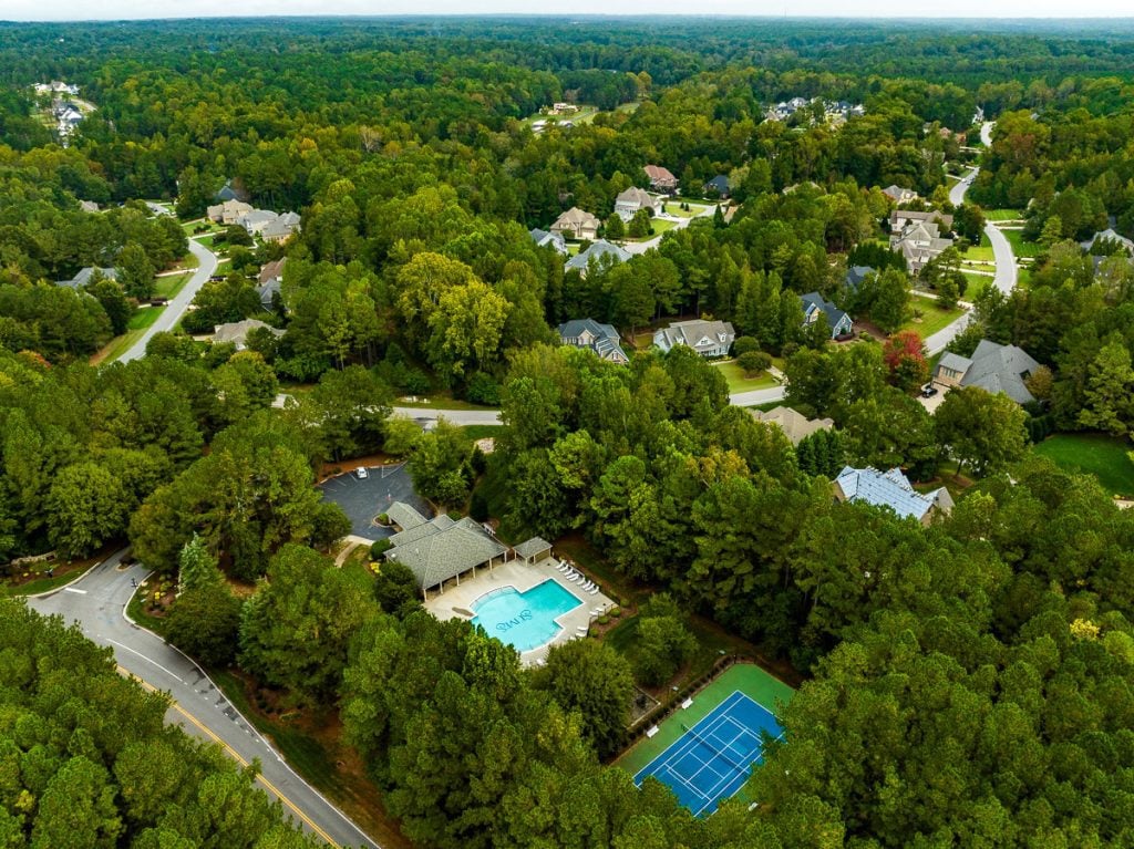 Aerial photo of houses in a neighborhood with green trees and a pool and tennis court.