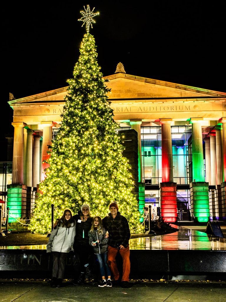 Family of four getting a photo taken in front of a Christmas tree.