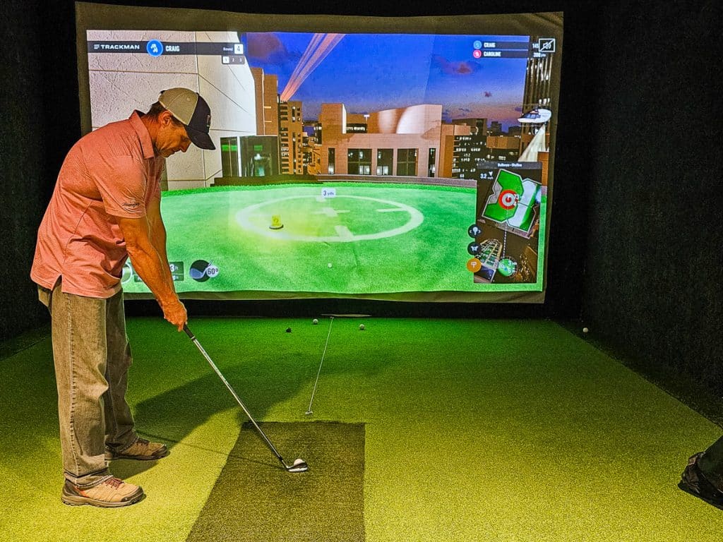 Man about to hit a golf ball against a screen.