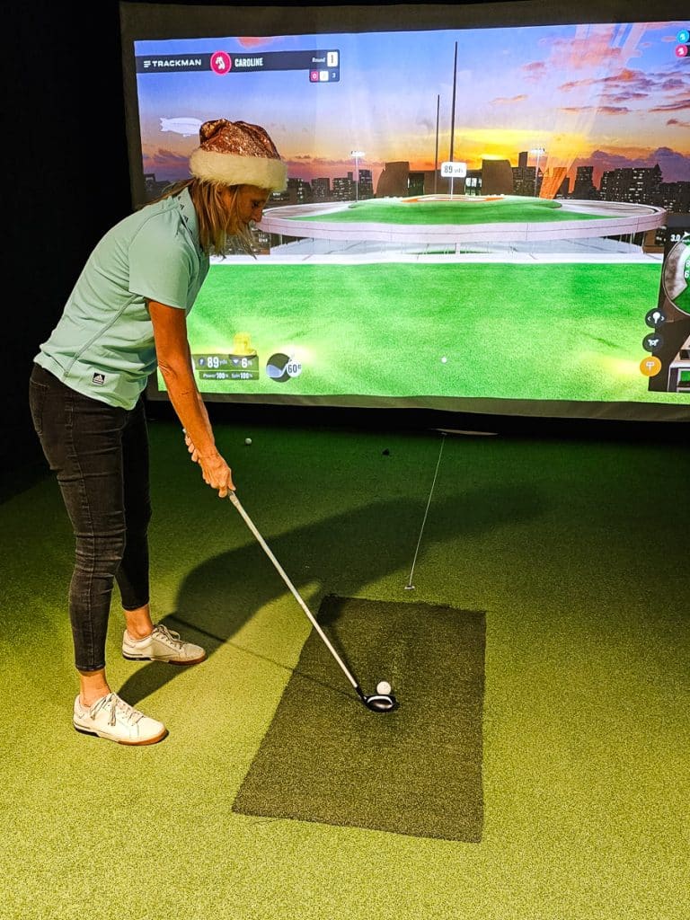Woman about to hit a golf ball against a screen.