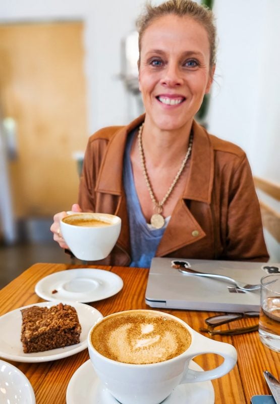 Lady sitting in a cafe drinking coffee and a slice of cake.