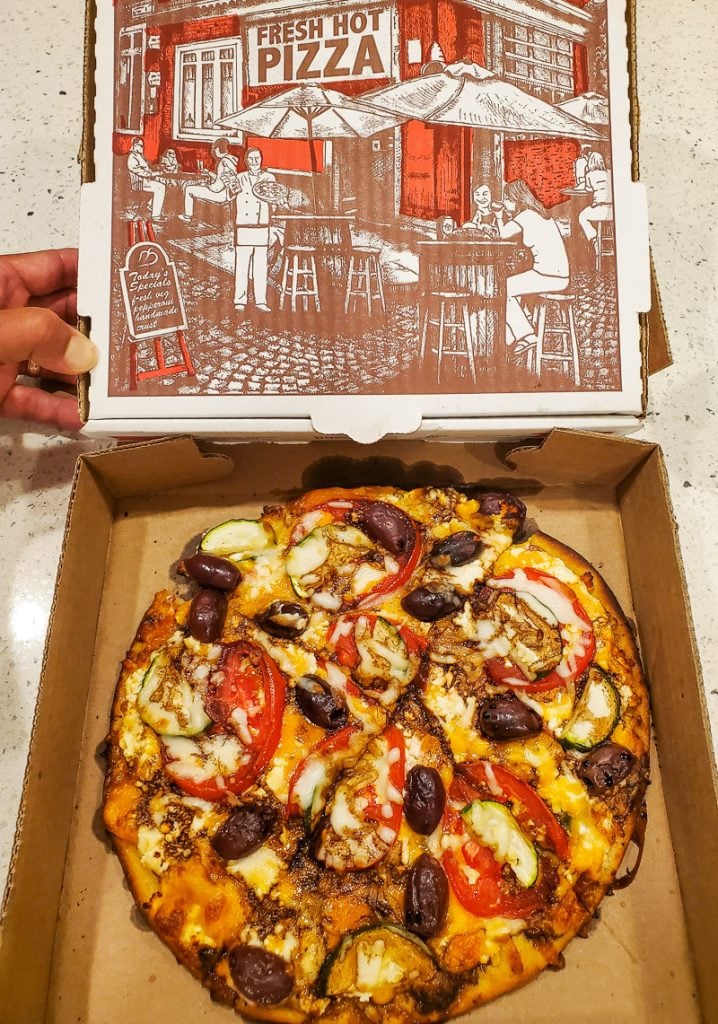 Pizza with olives, tomatoes and cheese inside a cardboard box.