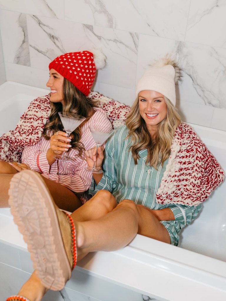 Two ladies sitting in a bathtub modeling clothes.