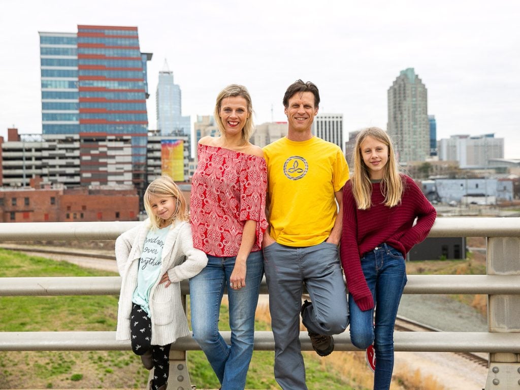 Family of four getting a photo taken with the Raleigh city skyline in the background.