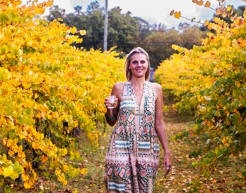 woman walking through vineyard with wine glass in hand smiling at camera