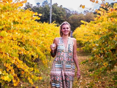 woman walking through vineyard with wine glass in hand smiling at camera