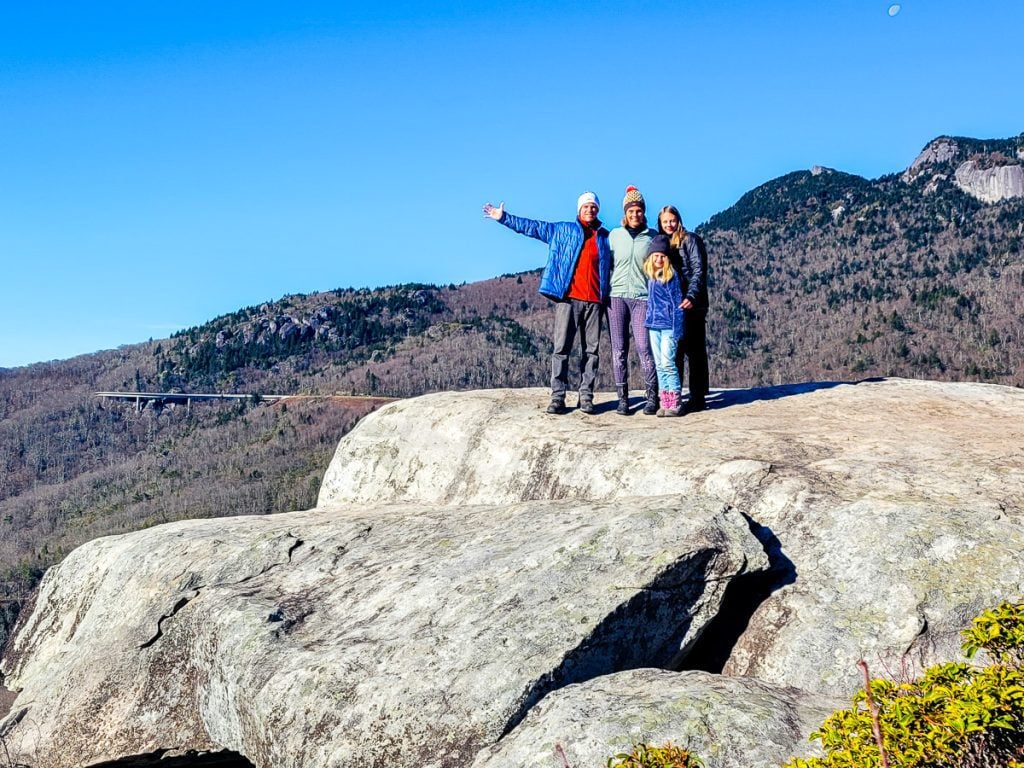 Family of 4 standing on a large rock with mountains in the background.