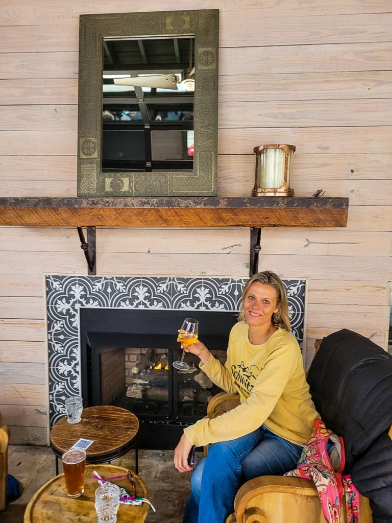 A woman sitting on a couch in front of a fire drinking wine.