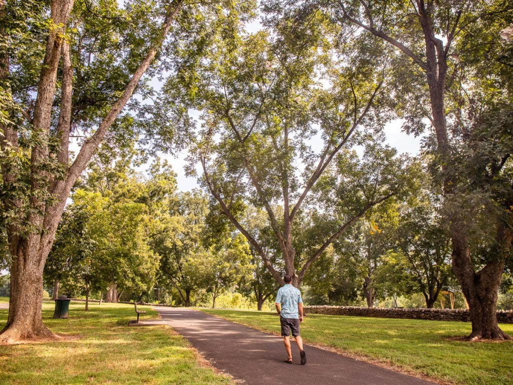 Man walking along a path in a park surrounded by trees.