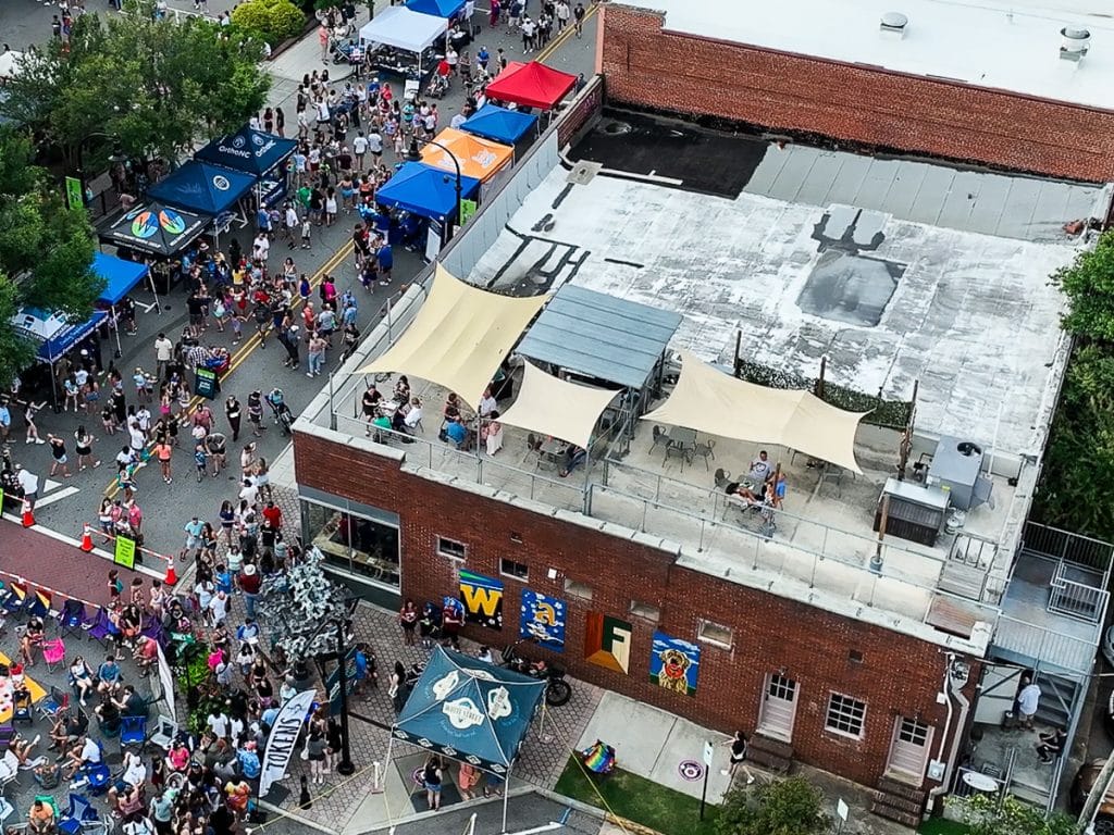 People sitting on a rooftop patio overlooking a street festival below.