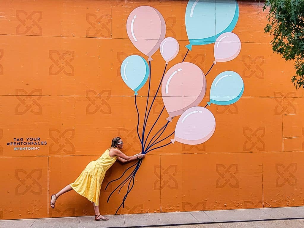 Woman standing next to a mural holding balloons.