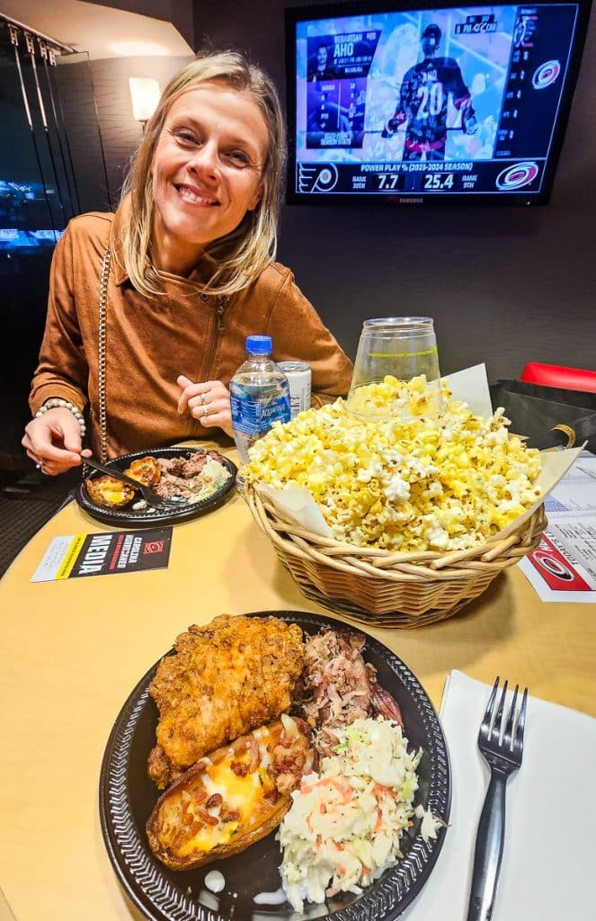 Lady eating a plate of food inside a suite at a sports arena.