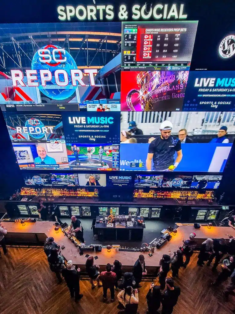 Large TVs in a sports bar and people drinking at the bar.