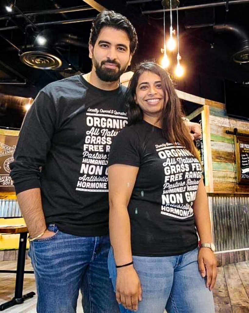 Man and woman standing in a restaurant for a photo wearing black t-shirts.
