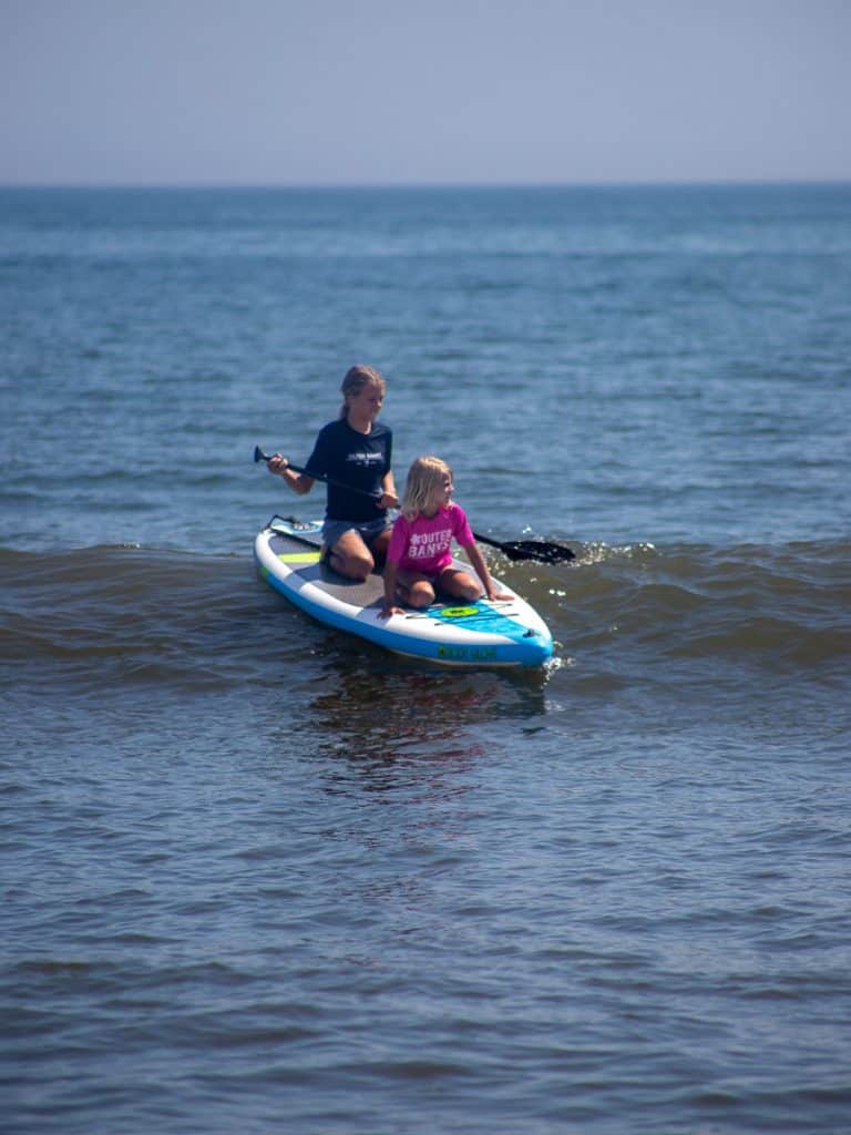 Two kids on a stand up paddle board.