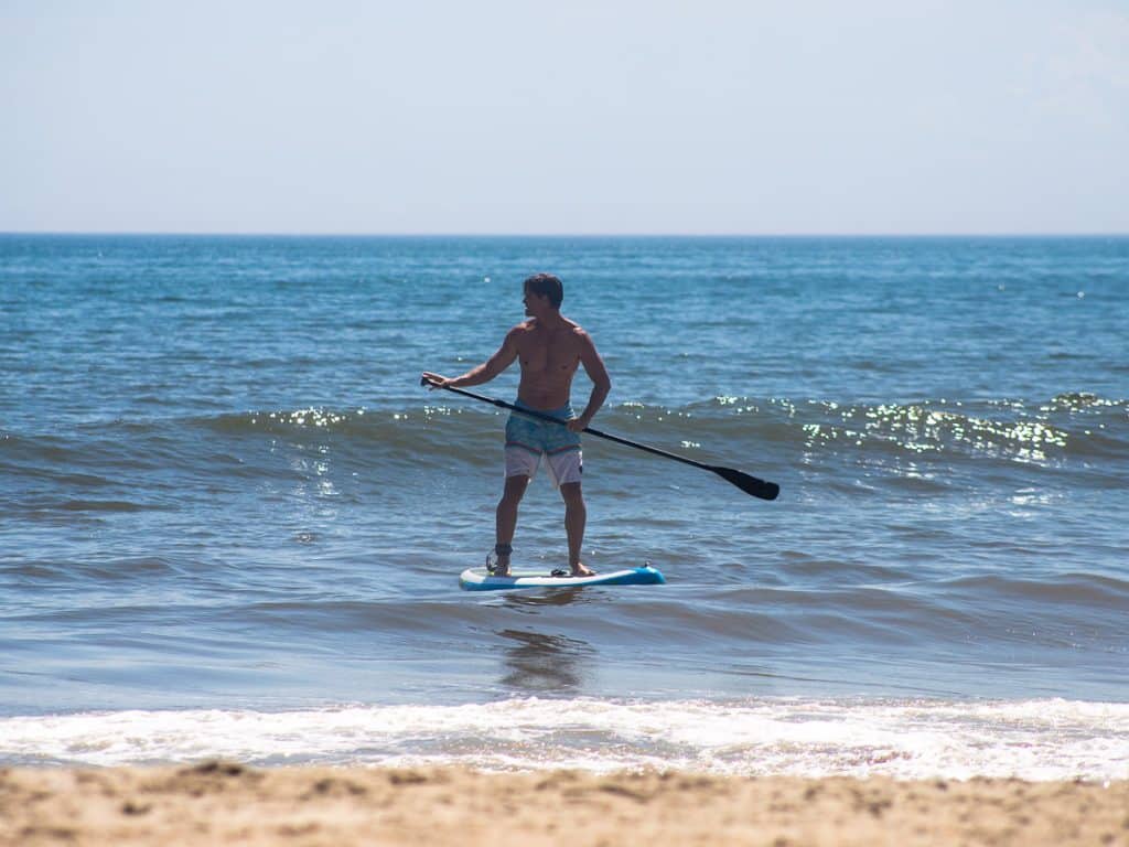Man riding a stand up paddle board at the beach.
