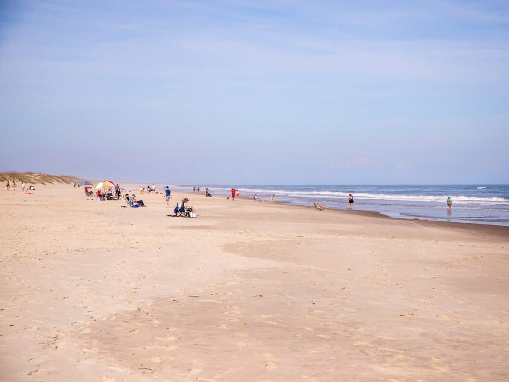 People siting on a beach and walking on the sand.