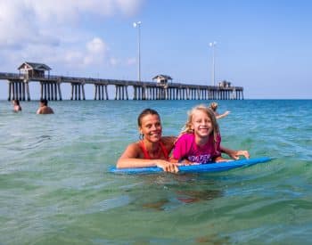 Mom and daughter swimming in the ocean with a body board.