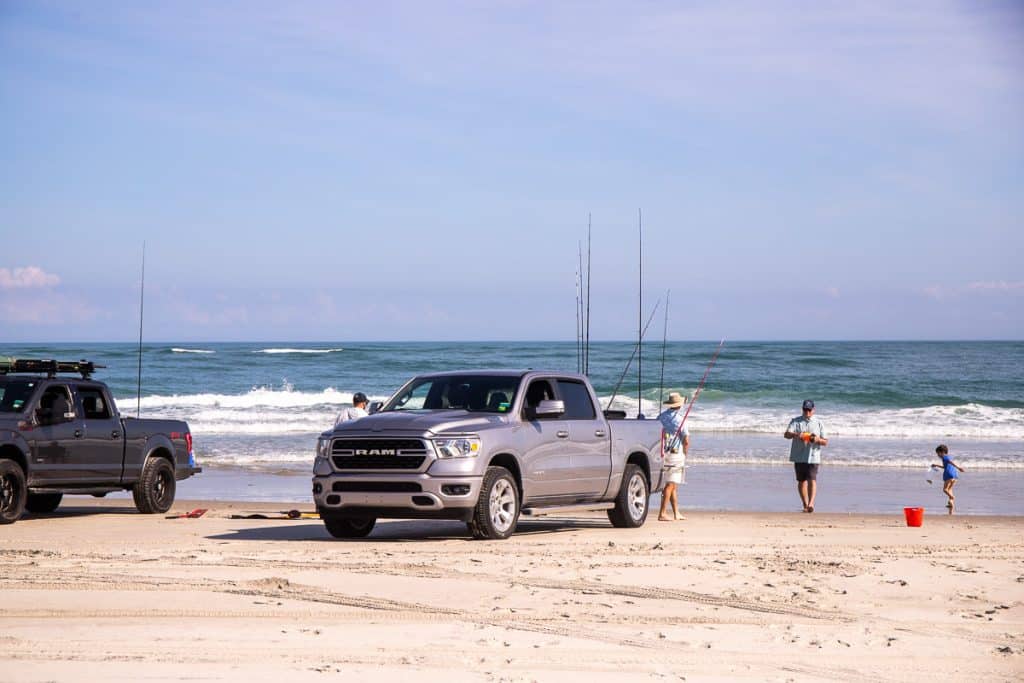 People beach fishing standing next to their trucks on the sand.