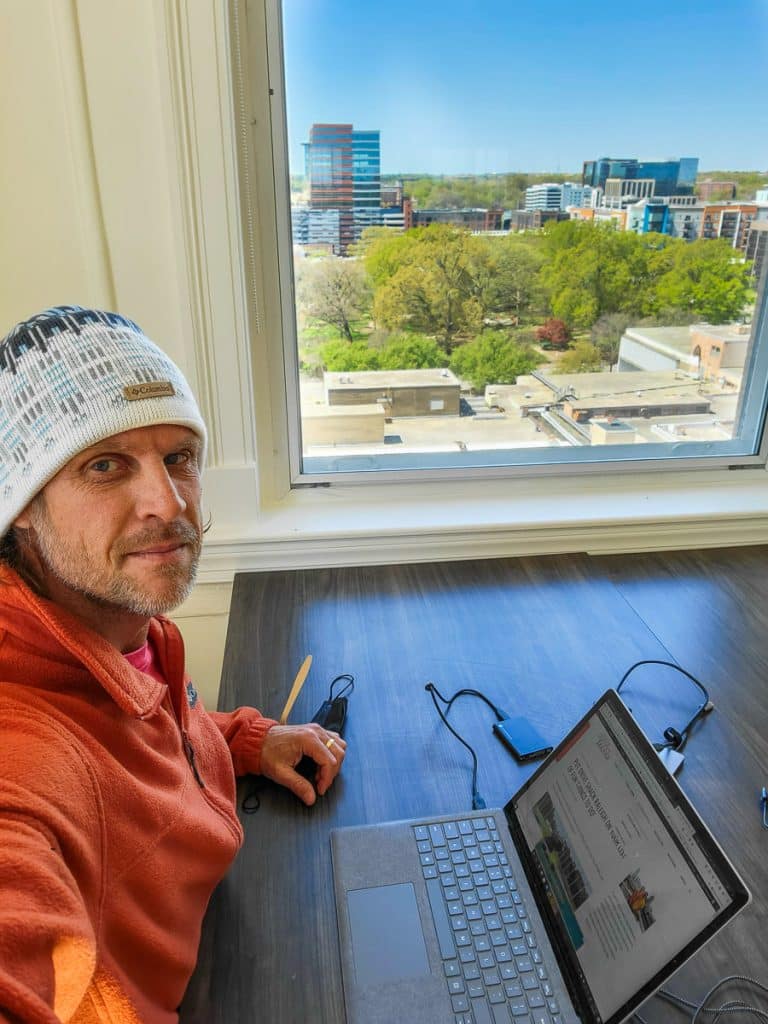 Man working on a computer with a window view of a park.