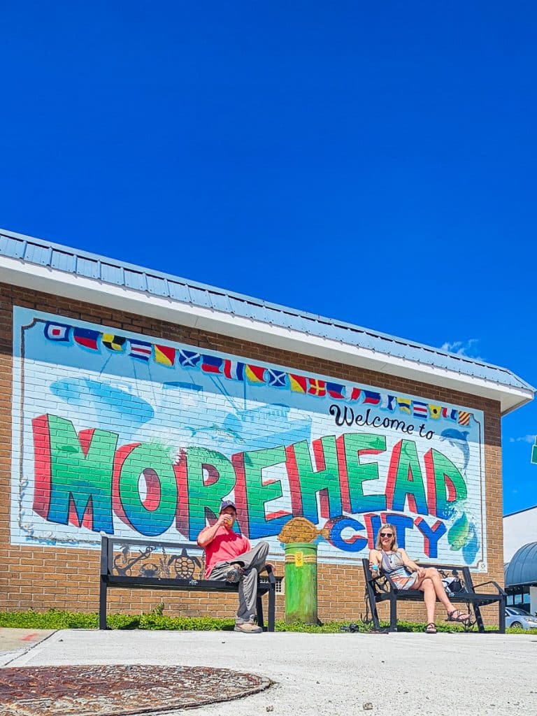 Man and woman sitting on a seat in front of a mural that says Morehead City.