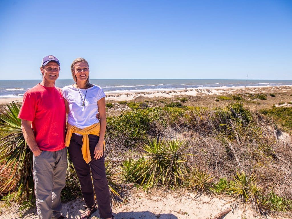 Man and woman standing on a sand dune overlooking the ocean.