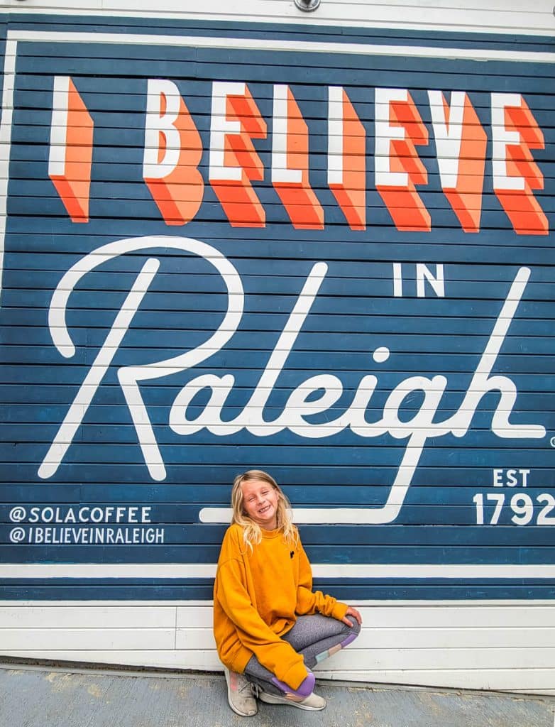 girl in front of i believe in raleigh mural