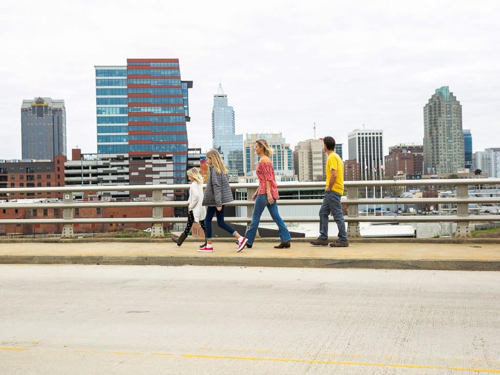Family of four walking across a bridge with a city skyline background.