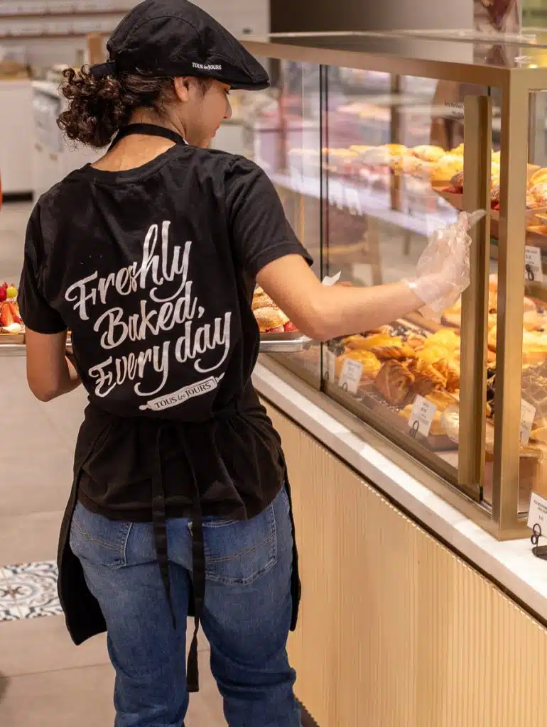 woman with tous les jours shirt on stocking bakery shelves