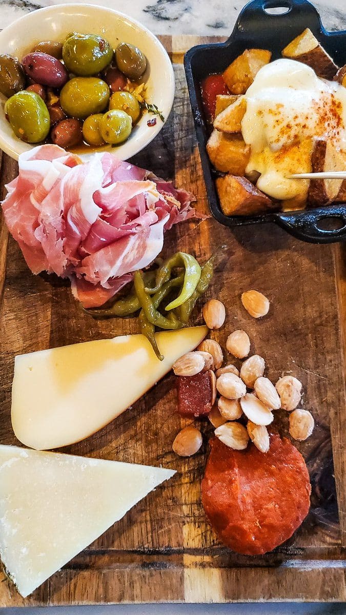 Charcuterie board of cheeses, olives, meats, nuts, and potatoes.