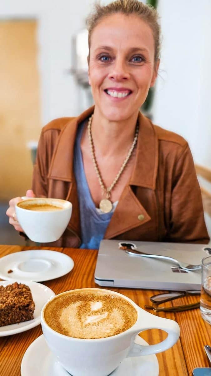 Lady sitting in a cafe drinking coffee and a slice of cake.