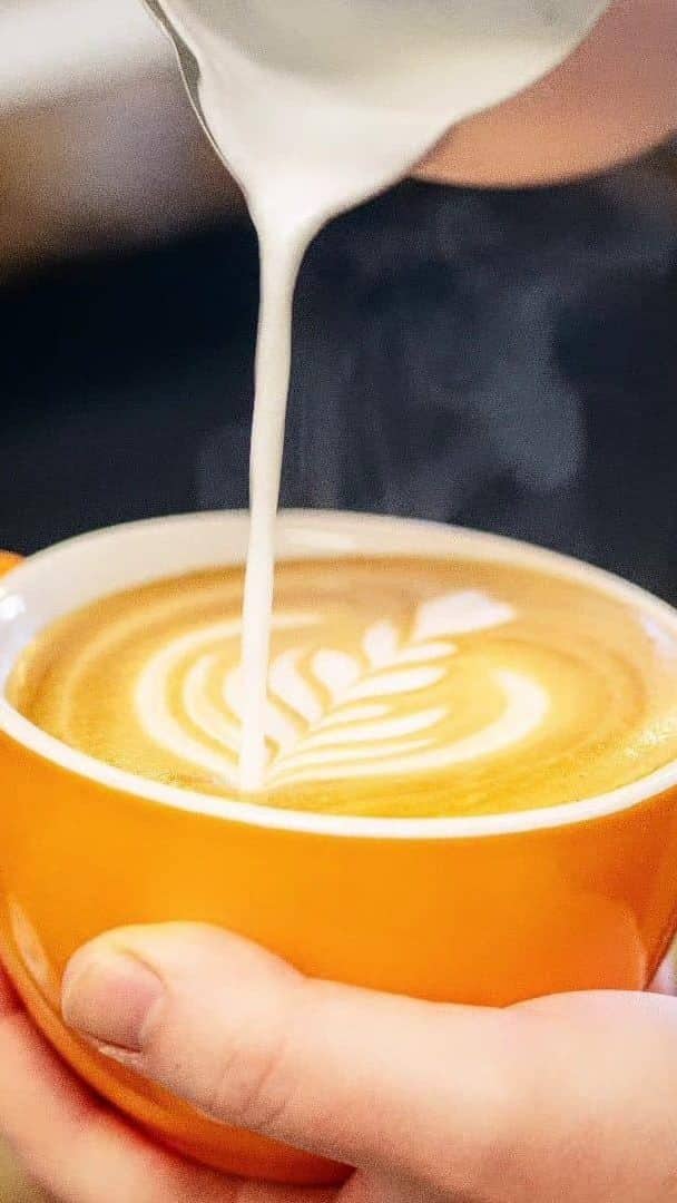 Hand holding a cup of coffee as milk being poured.